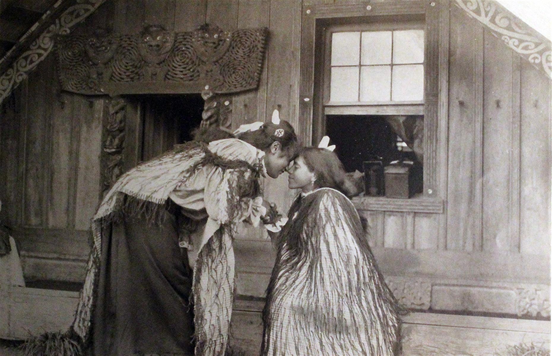 Māori girls meeting outside a traditional home