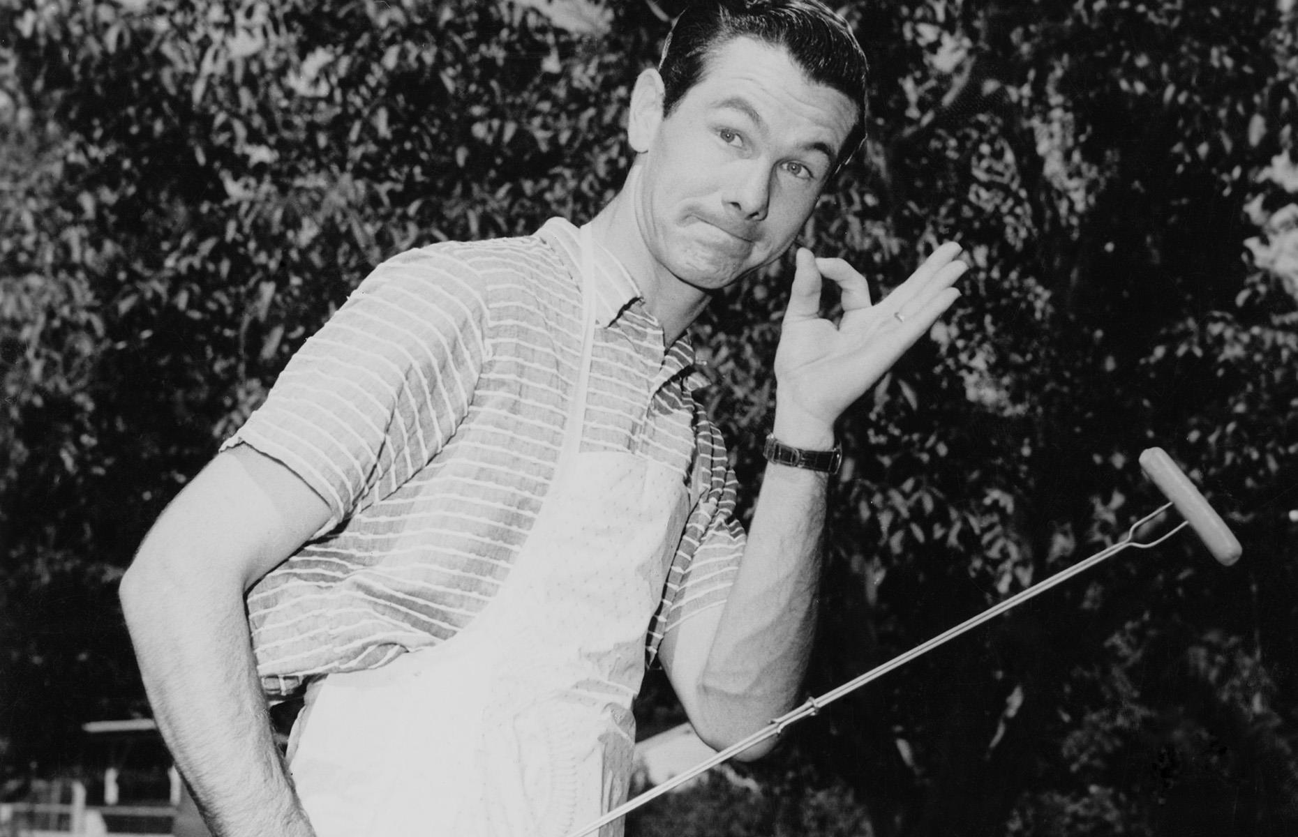 1955: Johnny Carson poses with a frankfurter